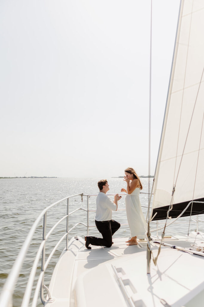 A pair standing together on a sailboat, celebrating their romantic surprise proposal.
