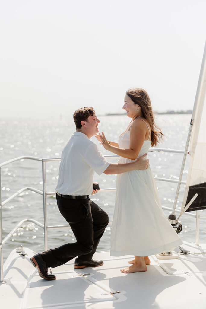 A pair standing together on a sailboat, celebrating their romantic surprise proposal.
