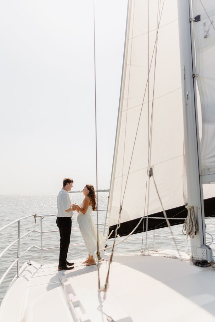 A joyful couple embracing after a surprise proposal on a sailboat in open water.