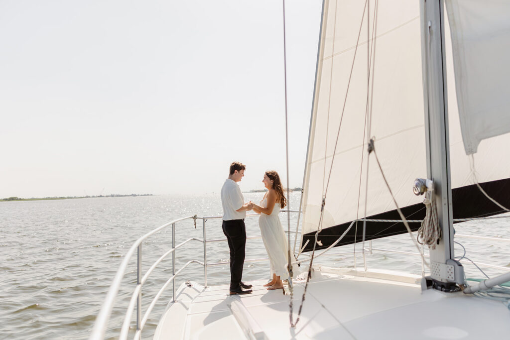 A joyful couple embracing after a surprise proposal on a sailboat in open water.
