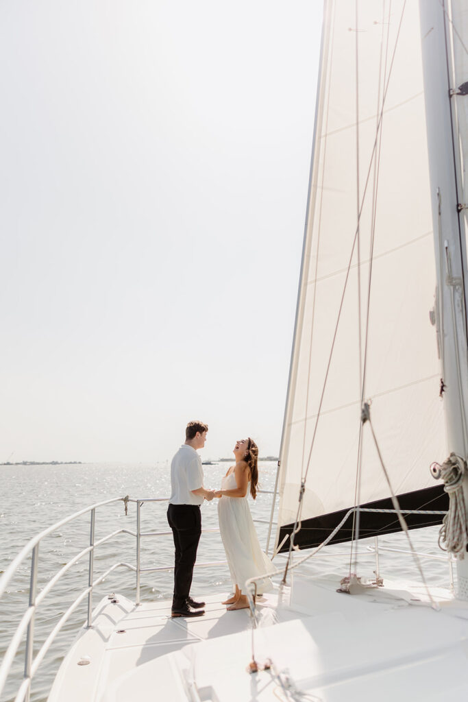 A joyful couple embracing after a surprise proposal on a sailboat in open water.
