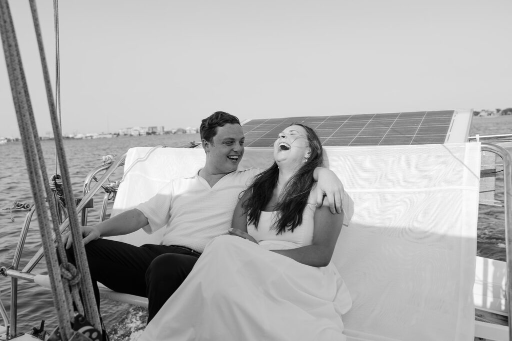 A pair standing together on a sailboat, celebrating their romantic surprise proposal.