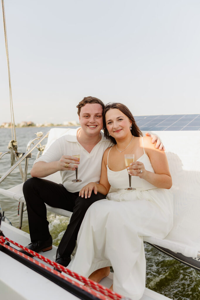 A pair standing together on a sailboat, celebrating their romantic surprise proposal.
