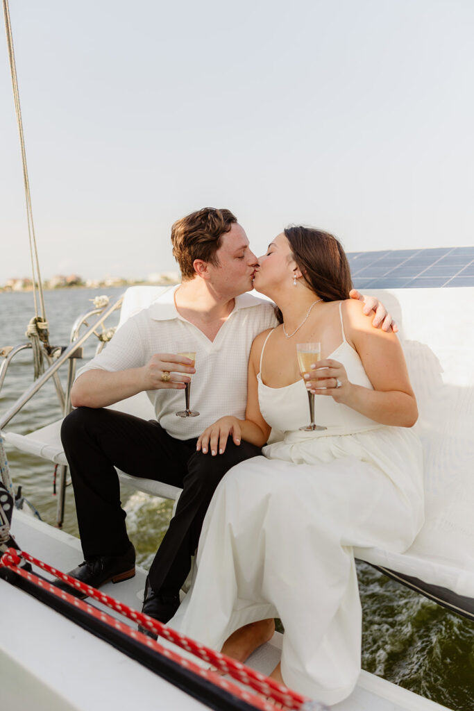 A pair standing together on a sailboat, celebrating their romantic surprise proposal.
