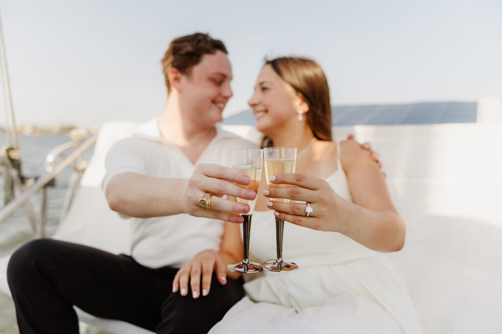 A pair standing together on a sailboat, celebrating their romantic surprise proposal.
