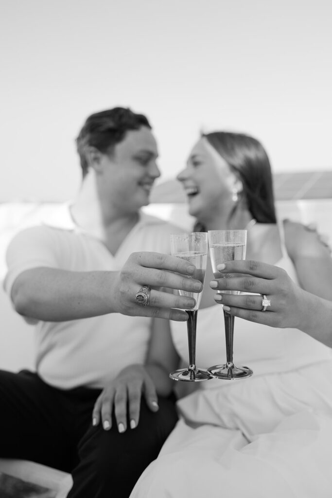 A pair standing together on a sailboat, celebrating their romantic surprise proposal.
