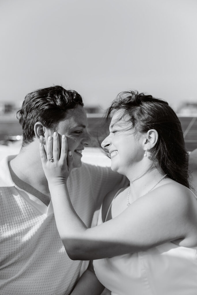 A pair standing together on a sailboat, celebrating their romantic surprise proposal.
