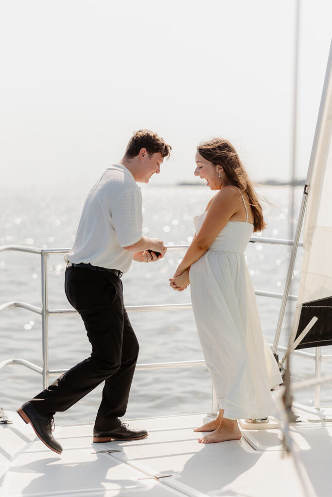 A joyful couple embracing after a surprise proposal on a sailboat in open water.
