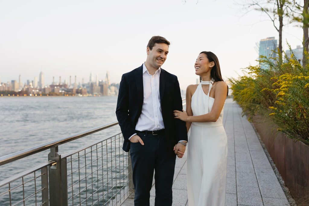 An engaged couple standing together in Domino Park, Brooklyn, as the sun begins to rise, capturing the peaceful vibe of the blue hour.