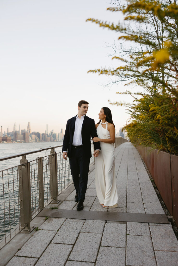 An engaged couple standing together in Domino Park, Brooklyn, as the sun begins to rise, capturing the peaceful vibe of the blue hour.
