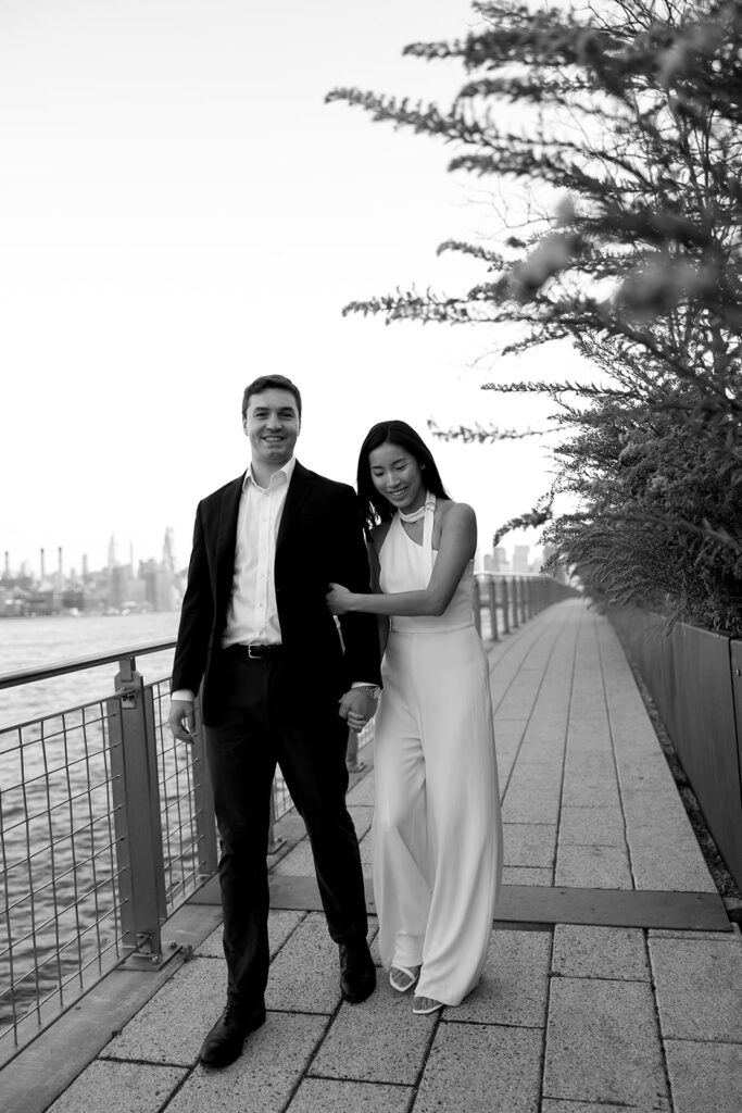 An engaged couple standing together in Domino Park, Brooklyn, as the sun begins to rise, capturing the peaceful vibe of the blue hour.
