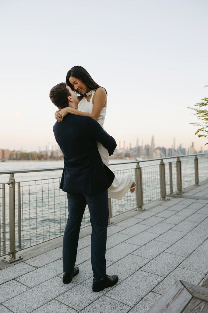 A pair embracing at Domino Park in Brooklyn during their sunrise engagement shoot, surrounded by a calm, pre-dawn atmosphere.
