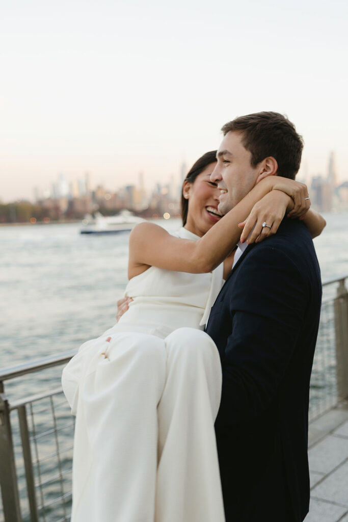 An engaged couple standing together in Domino Park, Brooklyn, as the sun begins to rise, capturing the peaceful vibe of the blue hour.
