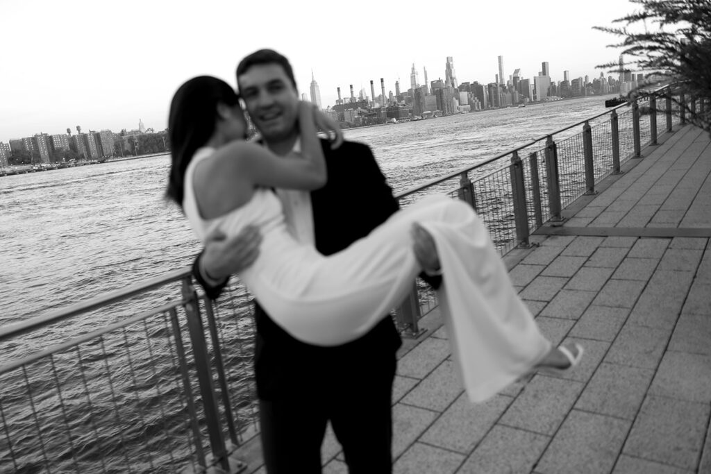 An engaged couple standing together in Domino Park, Brooklyn, as the sun begins to rise, capturing the peaceful vibe of the blue hour.
