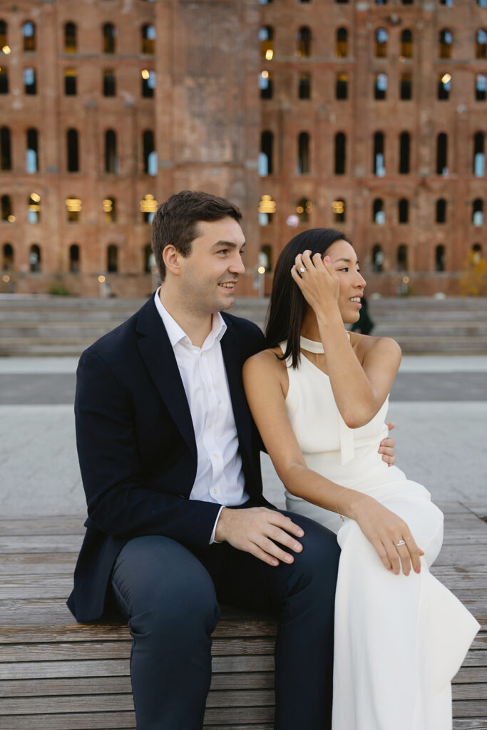 An engaged couple standing together in Domino Park, Brooklyn, as the sun begins to rise, capturing the peaceful vibe of the blue hour.
