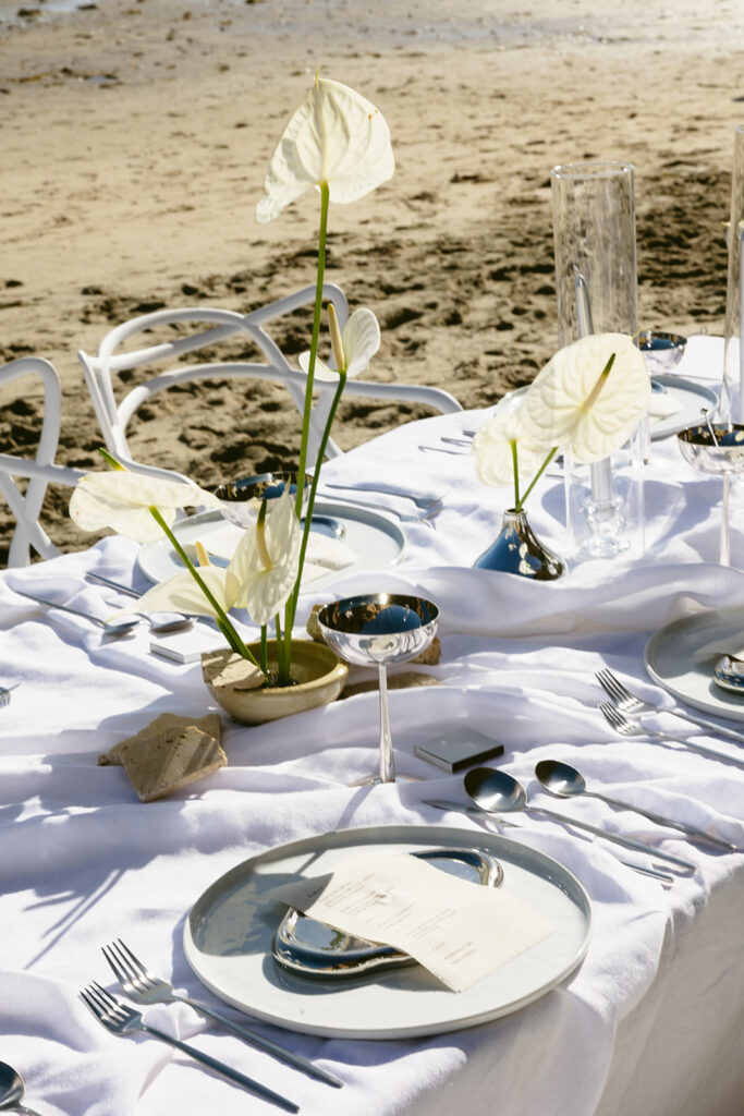 Modern coastal wedding table setup with silver flatware and linen decor
